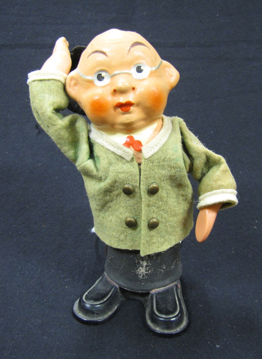 1 st. man hållande en hatt till hälsning. Inuti kroppen finns en fjäder som gör att mannen lyfter på hatten om man pressar ihop hans ben. Tillverkad av plast , metall och textil i Väst Tyskland av Rolly Toys på 1950-talet. H. 16 cm.