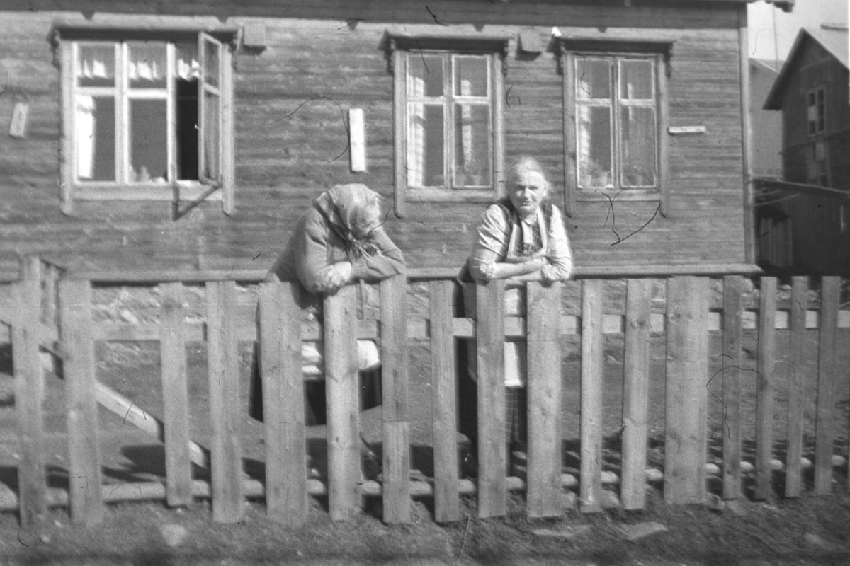 To damer står ved et gjerde en solskinnsdag i Vadsø. Damen til venstre på bildet heter Lydia, etternavnet er uskikkert, men hun var født Keskitalo. Ved siden av henne står Astrid Ballo.