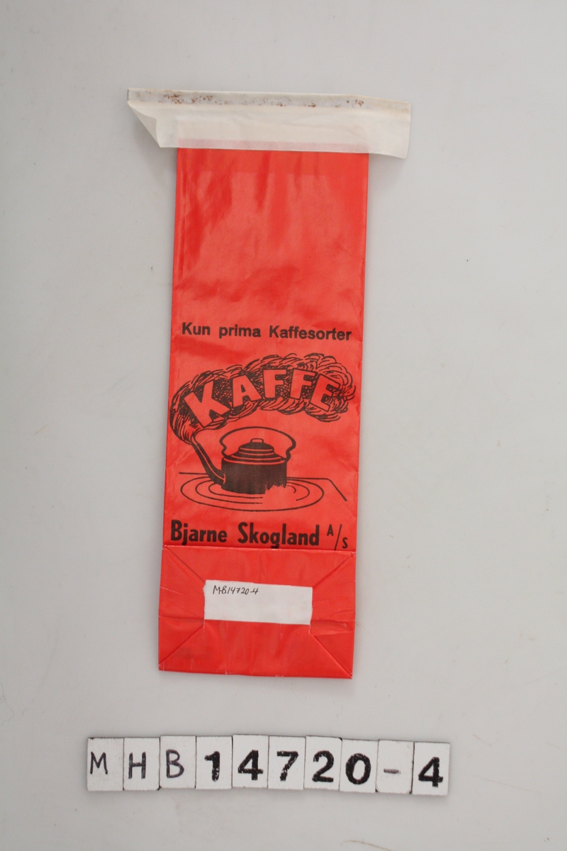 Kaffepose, rød bakgrunn, sort logo med skrift og en kokende kaffekjele. Hvit teip til lukking øverst.