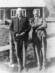 To menn ved gjerde, huset på Skogheim i bakgrunnen.