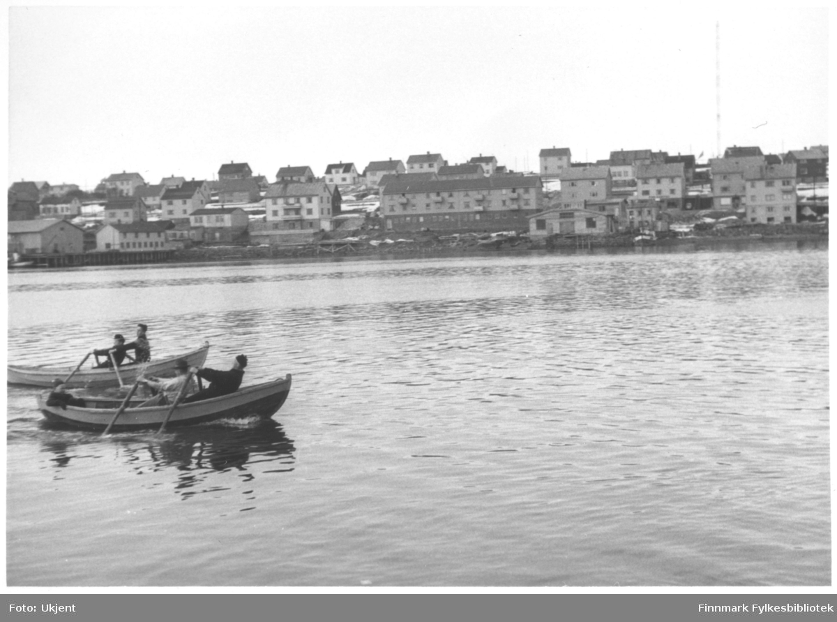 Bildet er muligens tatt 17.mai en gang på 1950-tallet. Påskrift på bildet er: 'kapproing 17.mai?'. På bildet kan man se to båter som ror side om side. I bakgrunen kan man se byen Vadsø. Det sitter to menn i hver av båtene.