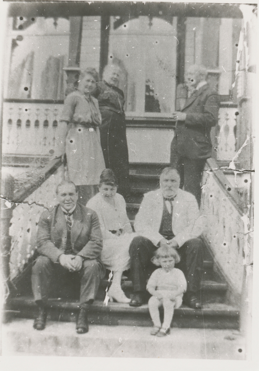 Sju personer på trappa foran Berlihuset. Mannen med skjegg identifisert som Børre Berli med kona Ellen til venstre.