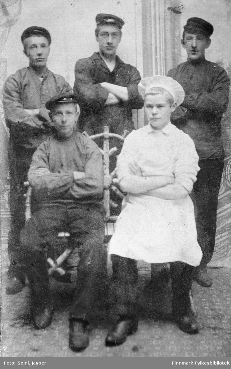 Gruppebilde av fem unge menn tatt hos fotografen Soini i Vadsø. Georg Bjerk og Edvard Pettersen sittende foran, den sistnevnte kledd som kokk, og J.Korbi, Eivind Riise og A.Hågensen stående bak dem. Bildet er tatt ca. 1905-1910.