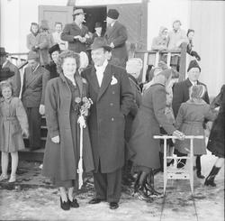 Et nygift par står foran kirketrappen, og gjestene strømmer 