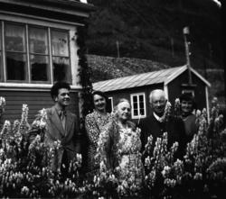 To menn og tre kvinner står ute i hagen utenfor stuevinduet.