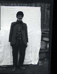 Portrett i helfigur av Ola Stølen, Vang, som står foran et l