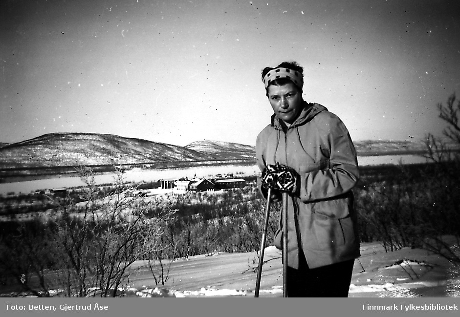 En kvinne, Hjørdis Amundsen, på skitur i Seida. Bak henne skimtes Seida internat og skole. Hjørdis jobbet som husmor på skolen i 50-tallet.