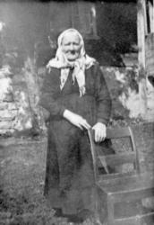 Eldre kvinne oppstilt ved stol foran en bygning, i hagen på 