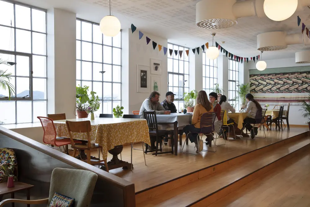 kafélokale med gjestar, stolar og bord, store fabrikkvindauge