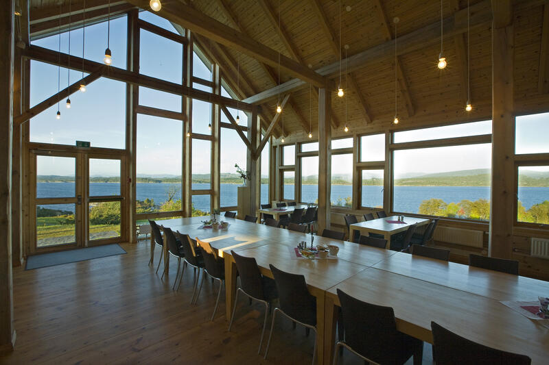 Interiør med langbord, vindauge med utsikt over kystlandskap. Foto