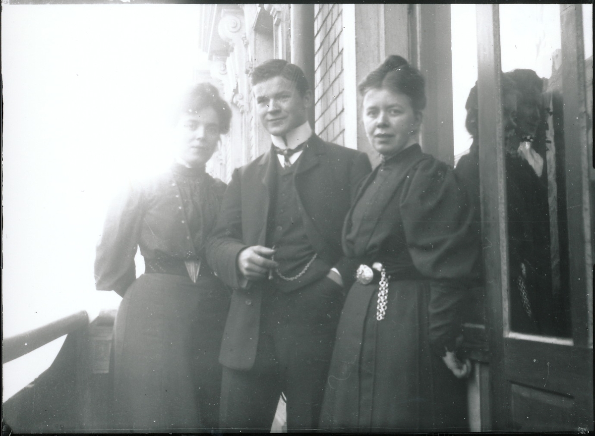 To unge kvinner og en ung mann på veranda til byhus.