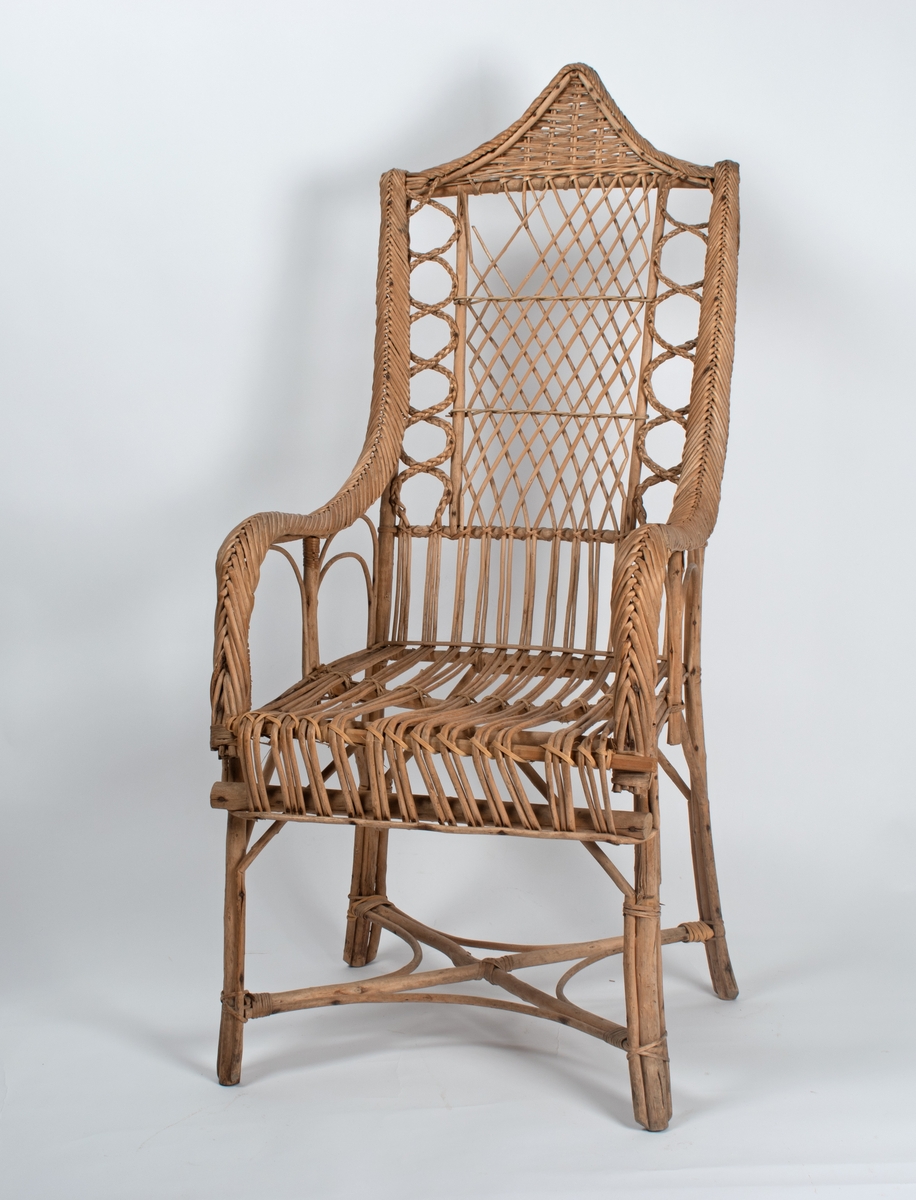 Kurvstol med høy rygg og armlener. Stolen har lett og åpen konstruksjon. Dekorative elementer med ulike typer fletting. Stolen har løs setepute og en liten, løs ryggpute.
