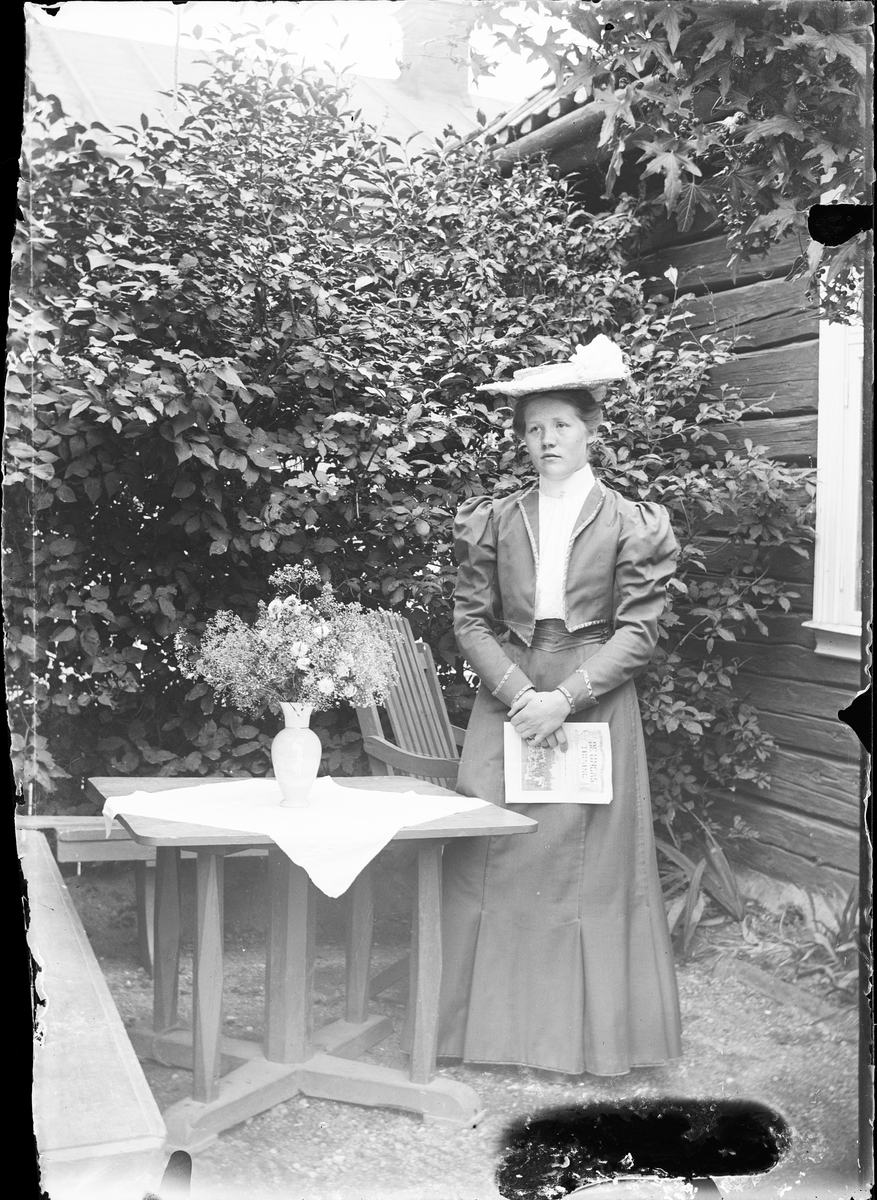 Ruth Skötsner vid bordet på uteplatsen med tidning i handen, Östhammar Uppland