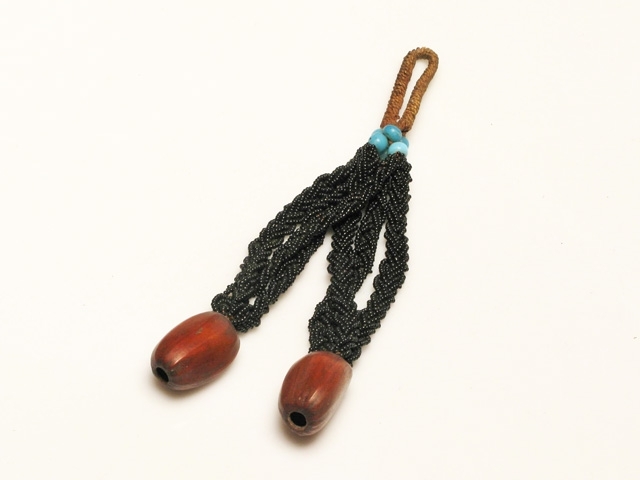 Halssmycke av två nötter fästa vid sex flätade svarta pärlband. Dessa är upptill sammanbundna med sex blå glaspärlor.