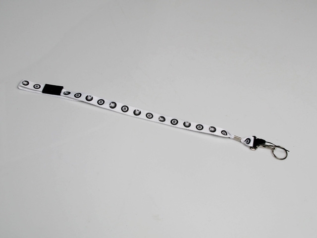 Nyckelhalsband med en längd på 53 cm. Vitfärgat band prytt med biljardbollar (alla är svart 8). Längst ut på halsbandet sitter ett spänne som håller fast en nyckelring.