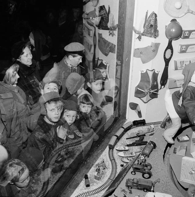 "Julskyltning hos Pilos Järnhandel". Barn utanför skyltfönstret tittar på leksakerna, tågbana båtar, bilar, traktor