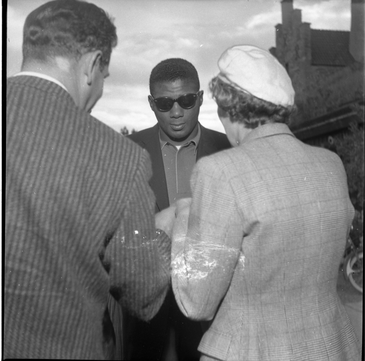 Boxaren Floyd Patterson i solglasögon skriver sannolikt autografer åt en man och en kvinna som står med ryggen mot fotografen. De befinner sig vid Gyllene Uttern strax söder om Gränna.