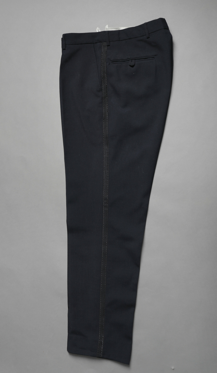 Svart uniformsbukse med påsydd blankt bånd i samme farge i sidene. Tilhører kelneruniform brukt på Sagafjord, Den norske Amerikalinje.