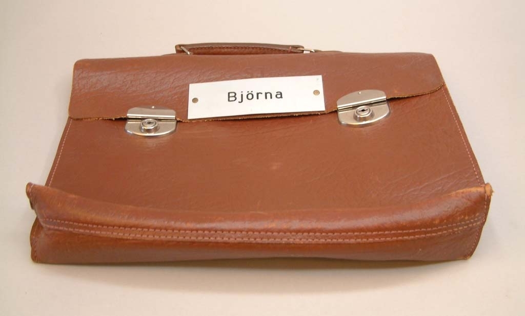 Stationsväska av brunt läder med två lås och två nycklar i portföljen.
Metallskylt med text "BJÖRNA".