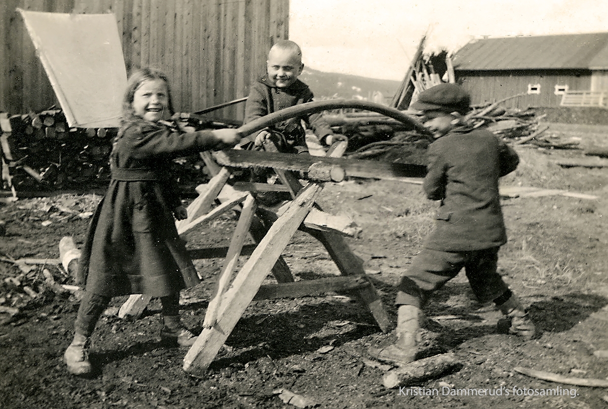 Sigrid, Olav og Kristian Dammerud sager ved hjemme på Ringvold, Bjørkelangen. I bakgrunnen låven til Anton B. Nilsen