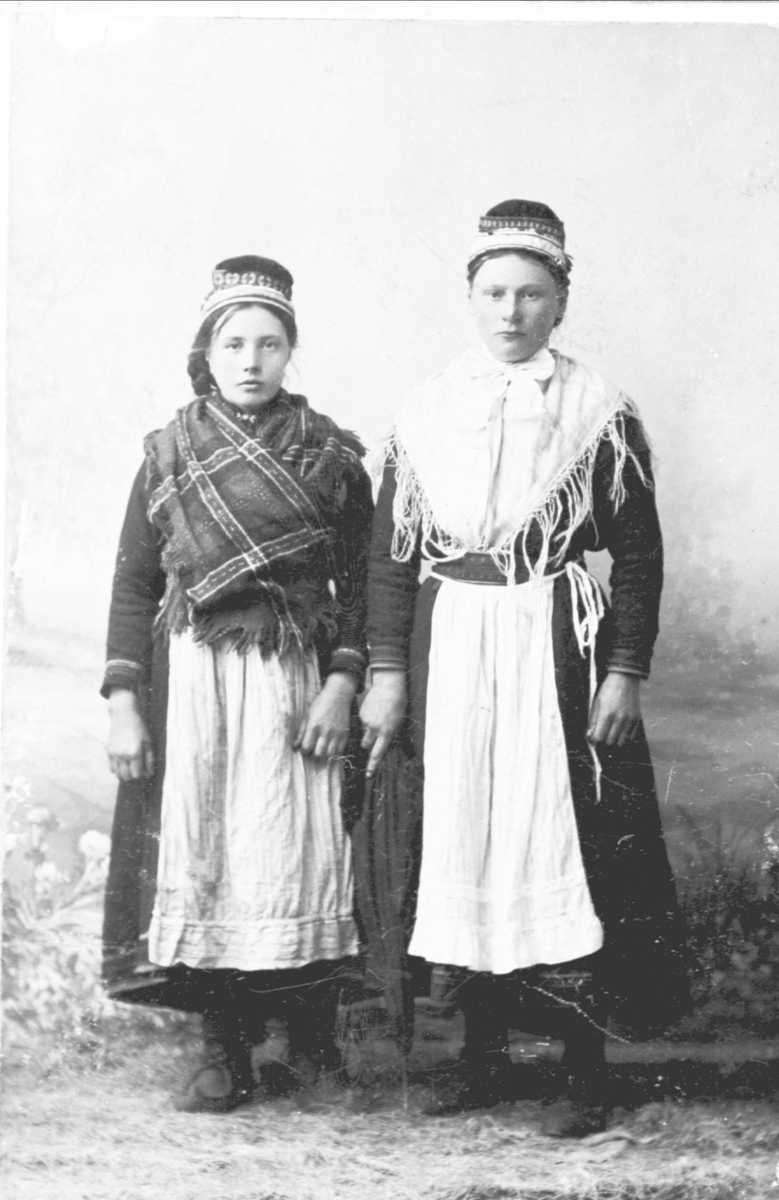 Studioportrett av to unge kvinner i helfigur med samisk drakt.