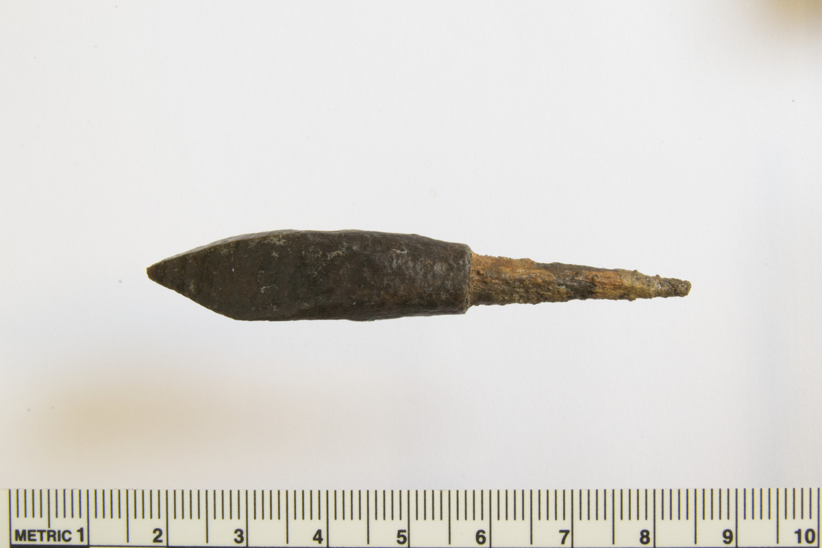 Armbrøstpil/bolt av jern, med firsidig tverrsnitt , stm.: 11x12 mm. L.: 72 mm, hvorav tange 28 mm. 