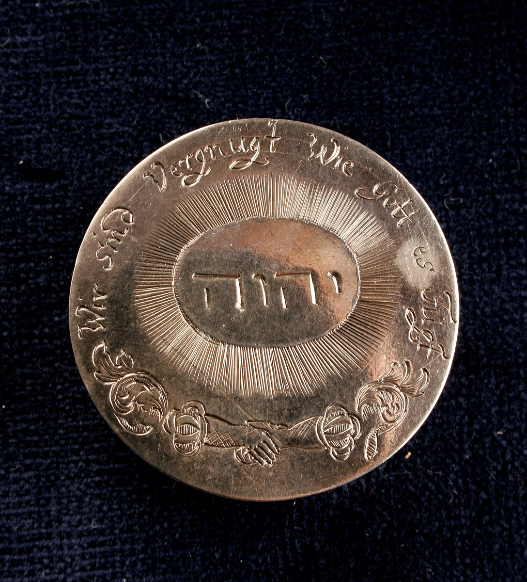 Ask med lock tillverkad av silver, med dekorationer på locket i form ingraverad text på hebreiska och tyska samt blomsterranka. Den tyska texten lyder "Wie sind Vergnugt wie Gott es Fugt".