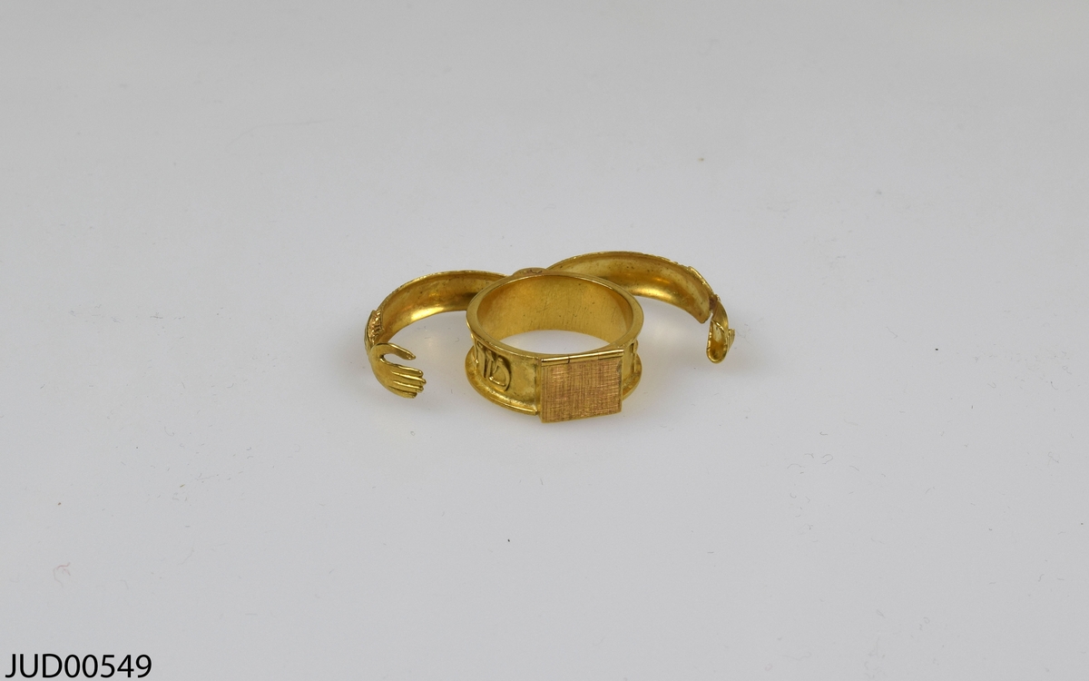 Guldpläterad silverring, med två händer hand i hand som går att öppna. Under finns en lucka som går att öppna, och inuti finns blå sten med hebreisk text i.