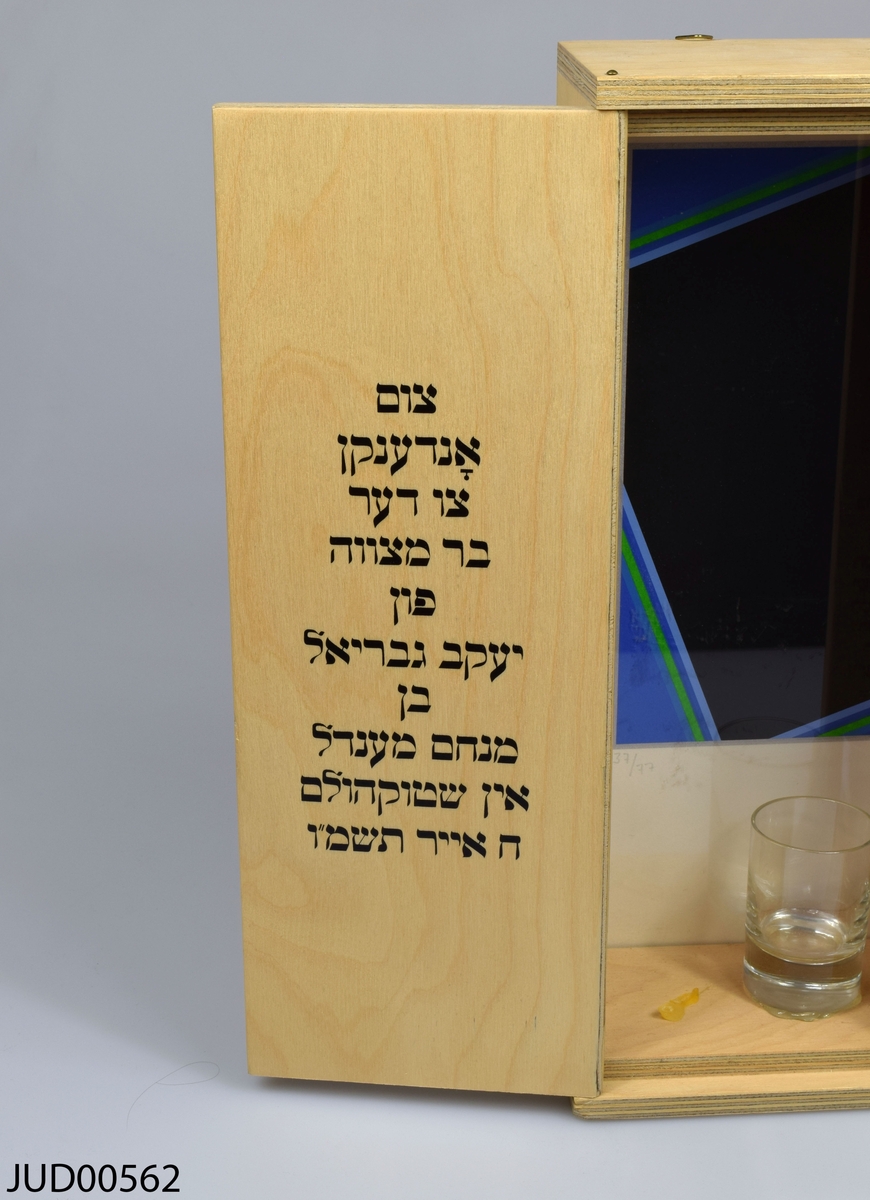 Låda tillverkad av trä för havdala (ceremonin som avsluter judiska sabbaten). Enkel och rak utformning. Öppning framtill med dubbla dörrar dekorerade med varsin davidsstjärna målad i svart. Inuti lådan finns tre små glas, kryddor och havdalaljus. Fonden är dekorerat med abstrakt geometrisk konst signerad Peter Freudenthal. På vänstra dörren dedikationstext på jiddisch, på högra dörren välsignelser för havdalaceremonin på hebreiska. Numrerad 37/77.