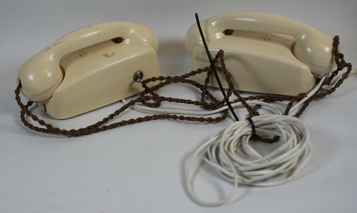 To telefonapparat forbundet med en kabel, hvorav en av disse har festebrakett for vegg.