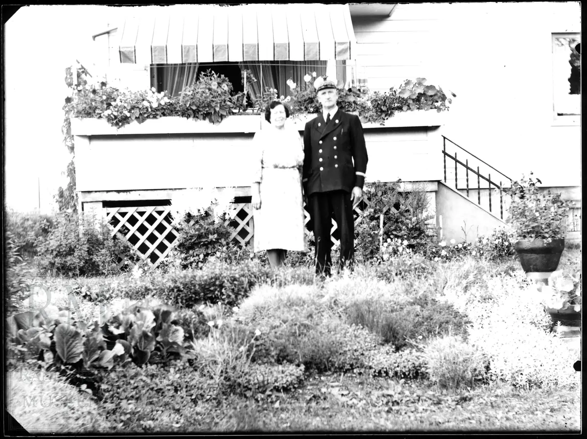 Et ektepar står ute i en hage foran et hus. Han er i jernbaneuniform.
