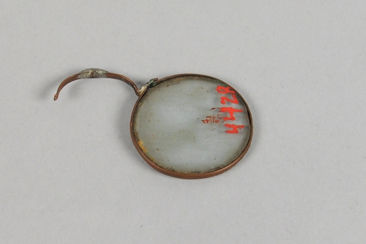 Ett brilleglass med metallinnfatning og del av en nesebøyle.