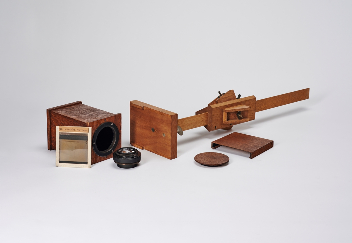 Bokskamera med objektiv, mattskive og stativ (mangler ben og kamera mangler en plateholder). Kamera er bygget av arkitekt Hans Grendahl (1877-1957). 
Objektivet er et Carl Zeiss Jena Tessar 1:45 F=18cm DRP.