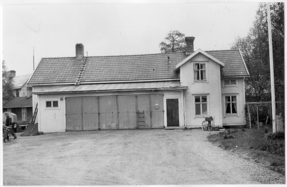Vägstation Y3, Matfors, filial Njurunda. Byggnad med garage i mitten, bostäder (två våningar) till höger. Moped och mansperson till vänster.