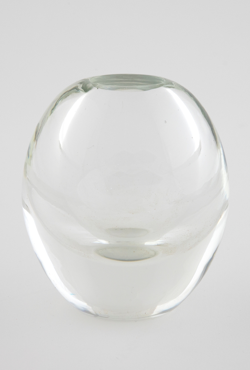 Ovalformet vase i tykt, klart glass med liten sirkulær åpning.
