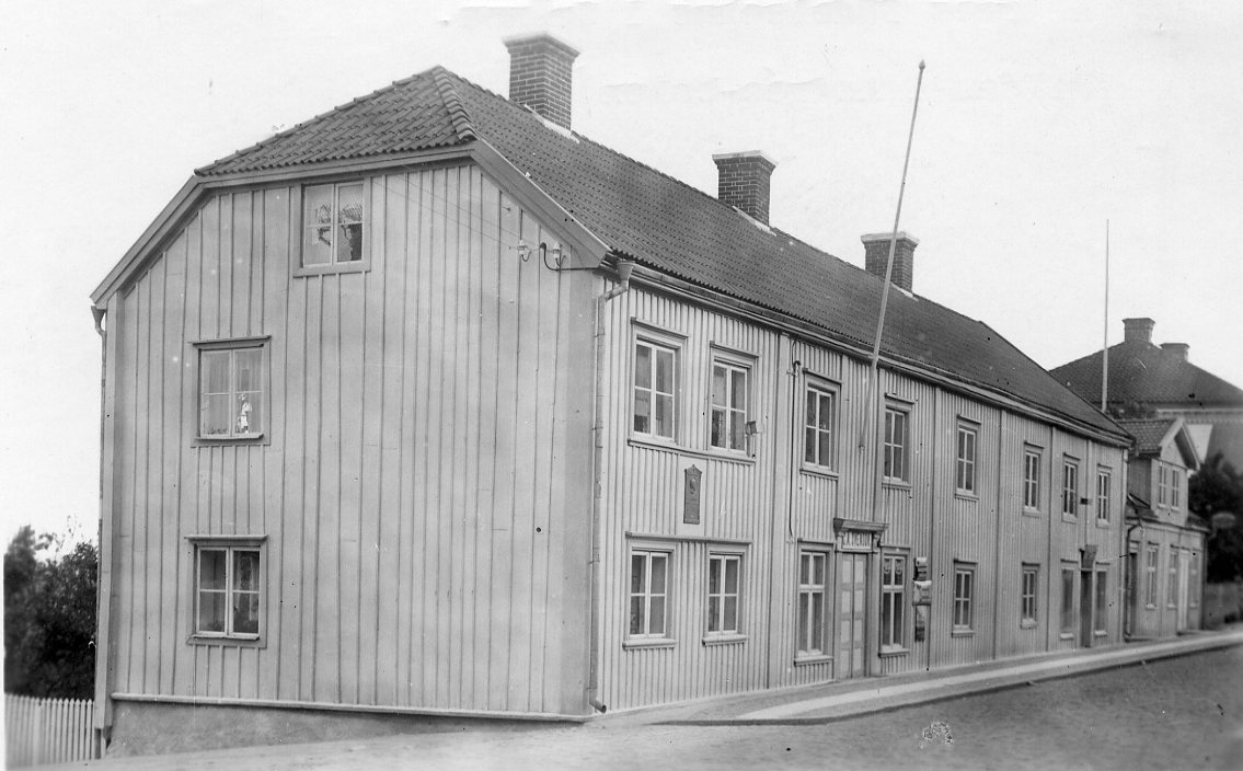 Brahegatan 37 i Gränna. En tvåvåningsbyggnad med locklistpanel och valmade gavlar. En fasadflaggstång ovanför port med skylt "C. A. Svensson", en speceri- och divershandel.