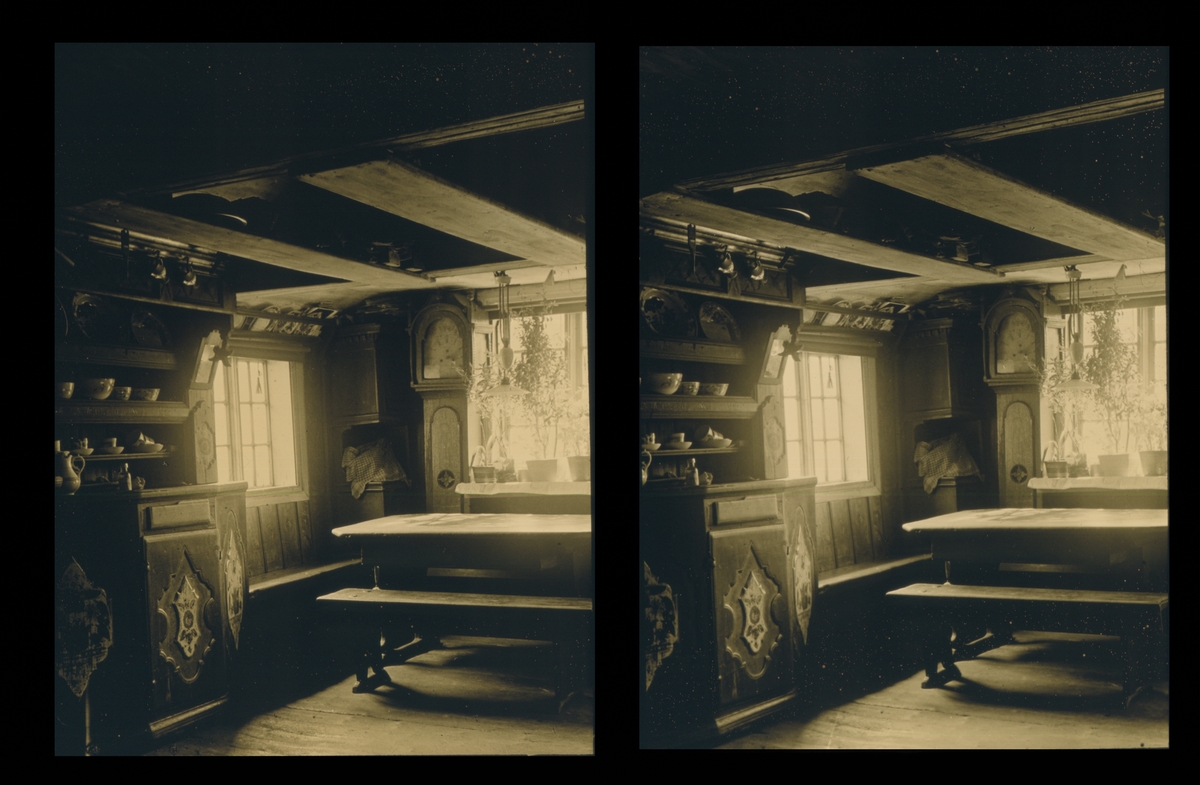 Interiør fra en stue. Fremskap, et firkantet hjørneskap og klokke. Bord og benker. Tilhører Arkitekt Hans Grendahls samling av stereobilder.