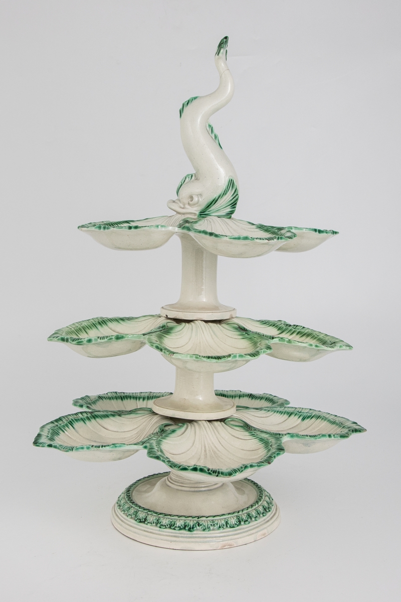 Bordoppsats/ etasjefat med palmetter, østersformede skåler og plastisk delfinfigur. Østersskålene er grønnglasert med en fjærrand.