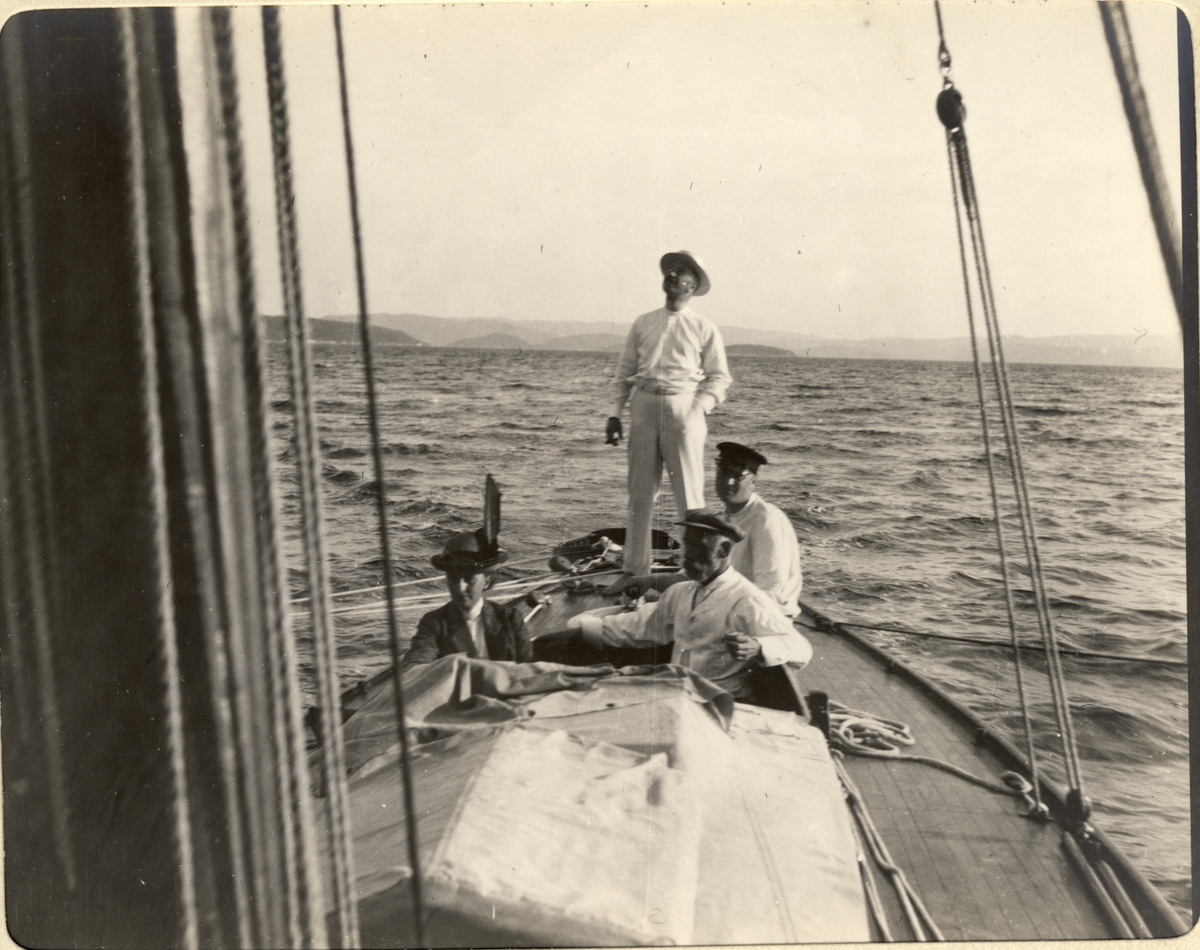 Fire personer i seilbåten «Morild» på vei fra Hankø ved Fredrikstad til Snarøya i Bærum. Til venstre Nini Egeberg, stående Westye P. Egeberg  sittende bak Oscar Egeberg. og foran Ferdinand Egeberg. Fotografert 1913.