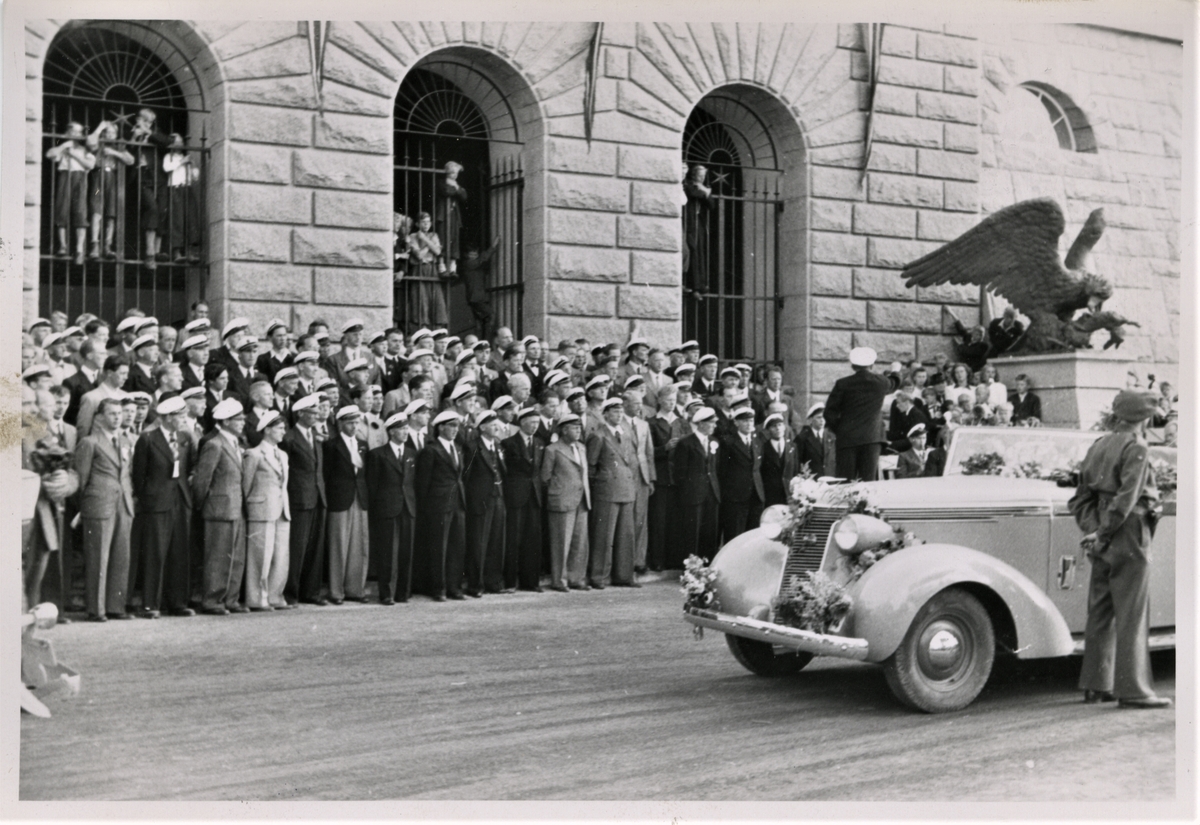 Kong Haakon VII besøker Haugesund den 22. august 1945. Her er "kongebilen" kommet til Rådhuset og Haugesund Sangerforbund har tatt oppstilling på Rådhustrappene og hilser kongen med "Norrønafolket".