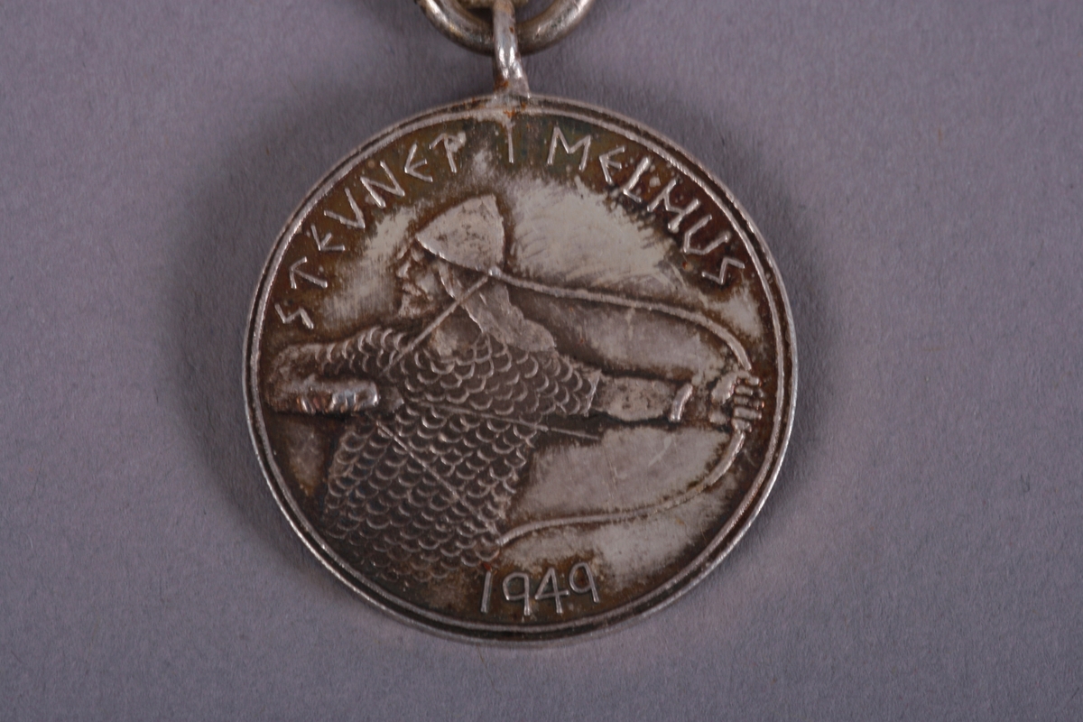 Medalje med hvitt bånd. Stevnet i Røros 1949 er skrevet rundt et portrett av en viking med bue. På baksiden en harpe med dragefjes ombranset av tekst og små blader. 
Teksten er: Orkla & Gauldal Sangerforbund.