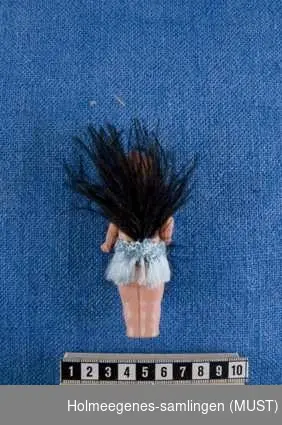 Fire Kewpiedukker, amerikansk av design, Rose O´ Neill, produsert i Japan. Kjennetegn for disse dukkene er sammenføyde ben, stive oppreiste armer, hodet har en liten støpt og malt hårtufs på hodet og over ørene, oppsperrede øyne (svart på hvitt) og sammenknepet smil. 
ST-K.HE.00900-1 er kledd i lysblå frynseskjørt med svart fjær, bak på ryggen svart strutsefjær. Grønnmalte øredobber.
STK.HE.00900-2 er kledd i drapert rosa hoftesjal med lyseblå sløyfe på magen, rosa turban og lyseblå sløyfe, grønnmalte øredobber.
ST-K.HE.00900-3 er kledd i drapert lilla hoftesjal med gul sløyfe, lilla turban med gul sløyfe, grønnmalte øredobber. 
ST-K.HE.00900-4 er kledd i lilla silke frynseskjørt med gule fjær foran og bak, grønnmalte øredobber.