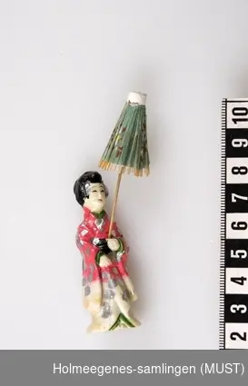 Liten japansk porselensdukke, kledd i kimono med liten grønn parasoll av rispapir.