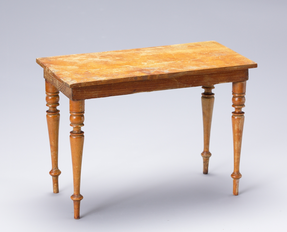 Ett dockbord i trä med svarvade ben. Bordet ingår i ett möblemang med två stolar.