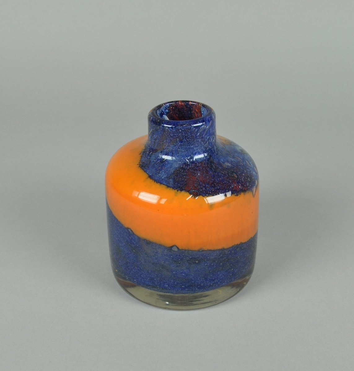 Munnblåst vase av glass. Rund sylindrisk form med lav hals. Vasen har spiralisert dekor i fargene oransje og blått.