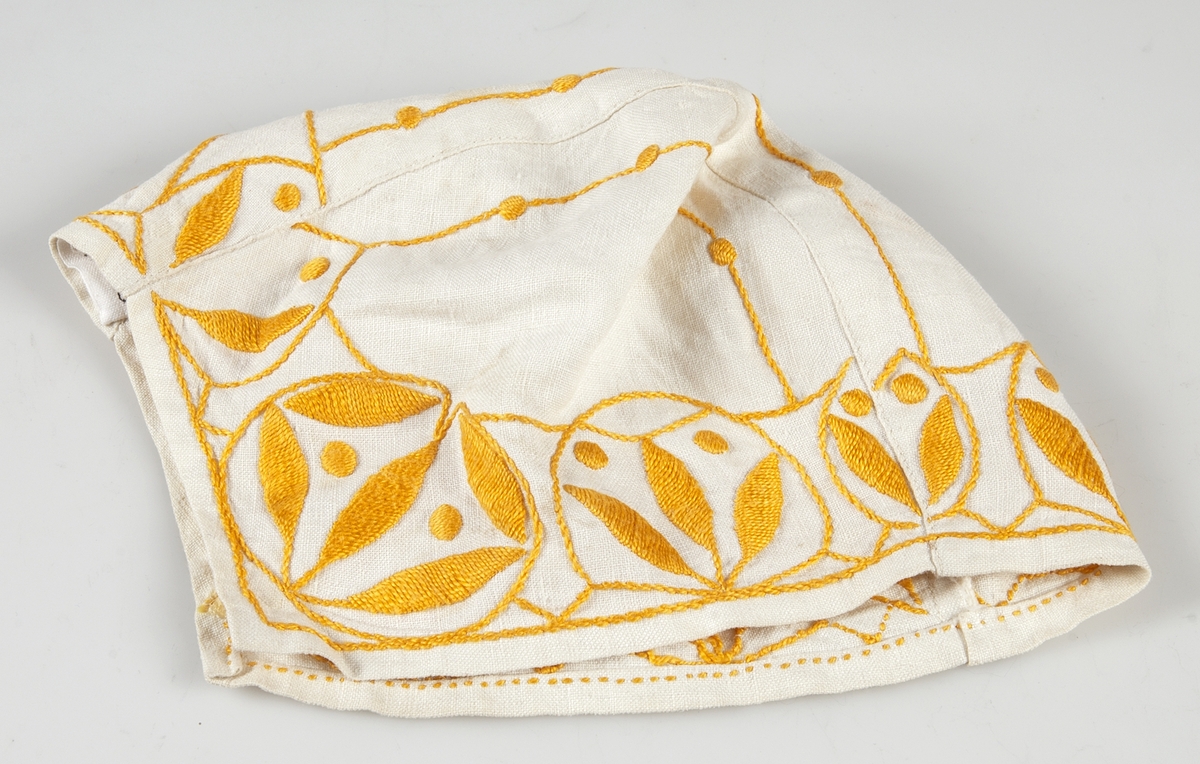 Mössa sydd av ett mittstycke med två sidostycken av vit linnelärft med broderi i plattsöm och stjälksöm av gul marcerisrérat bomullsgarn.