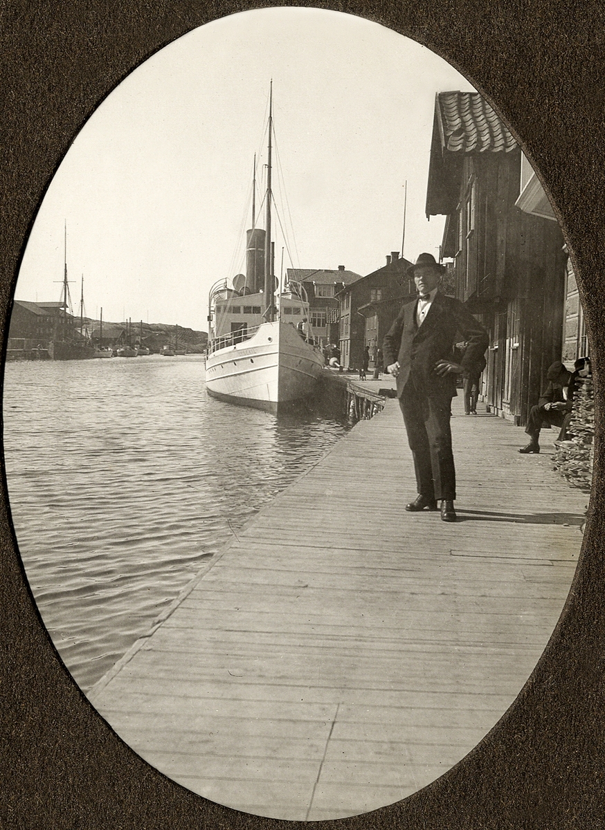 En man står på en långsträckt träbrygga på Smögen med en ångbåt, s/s "Lysekil", bakom sig.