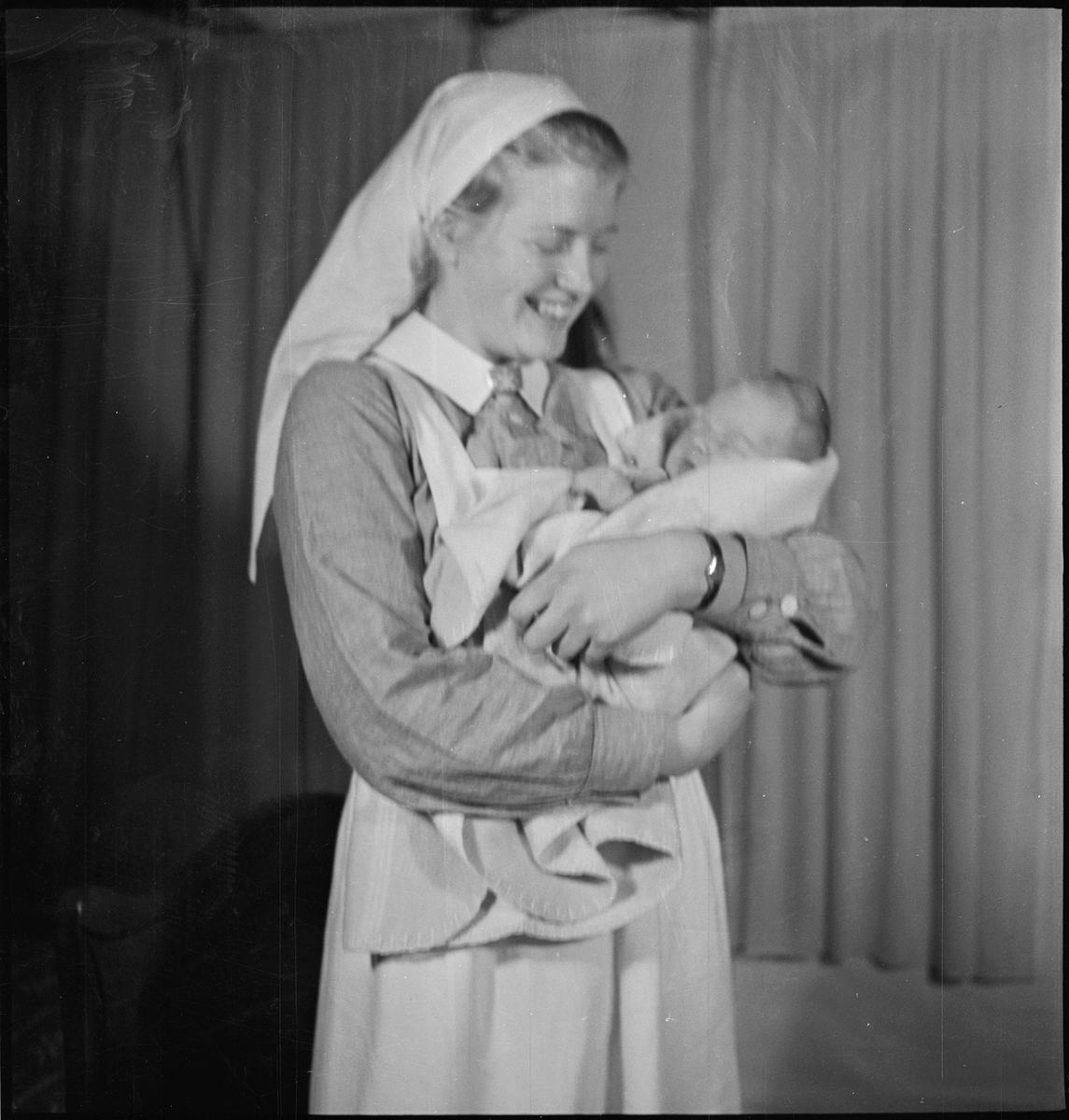 En kvinne med et nyfødt barn i armene. Bilde nr. 7 er av en barnepike med barnet i armene og bilde, 8 og 9 er av en stue med blomster og pynt i anledning den nyfødte.