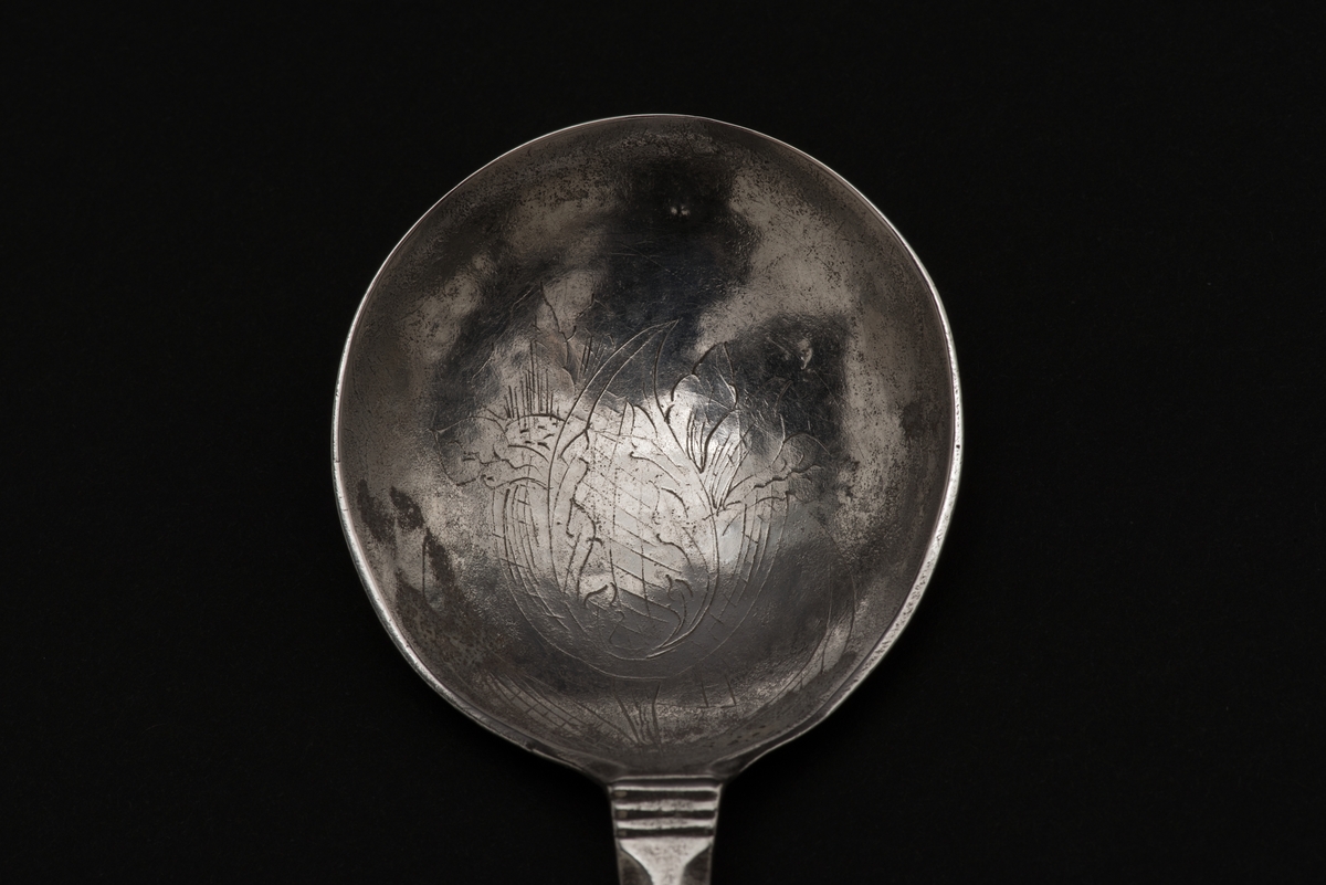 Supsked av silver med profilerat skaft och en dubbel kerubknopp, med ett stiliserat kerubansikte. 
Bladet är på insidan dekorerad med en graverad tulpan. 
Stämplarna på skaftets baksida visar att skeden är tillverkad av Erik Nordvall i Norrköping.