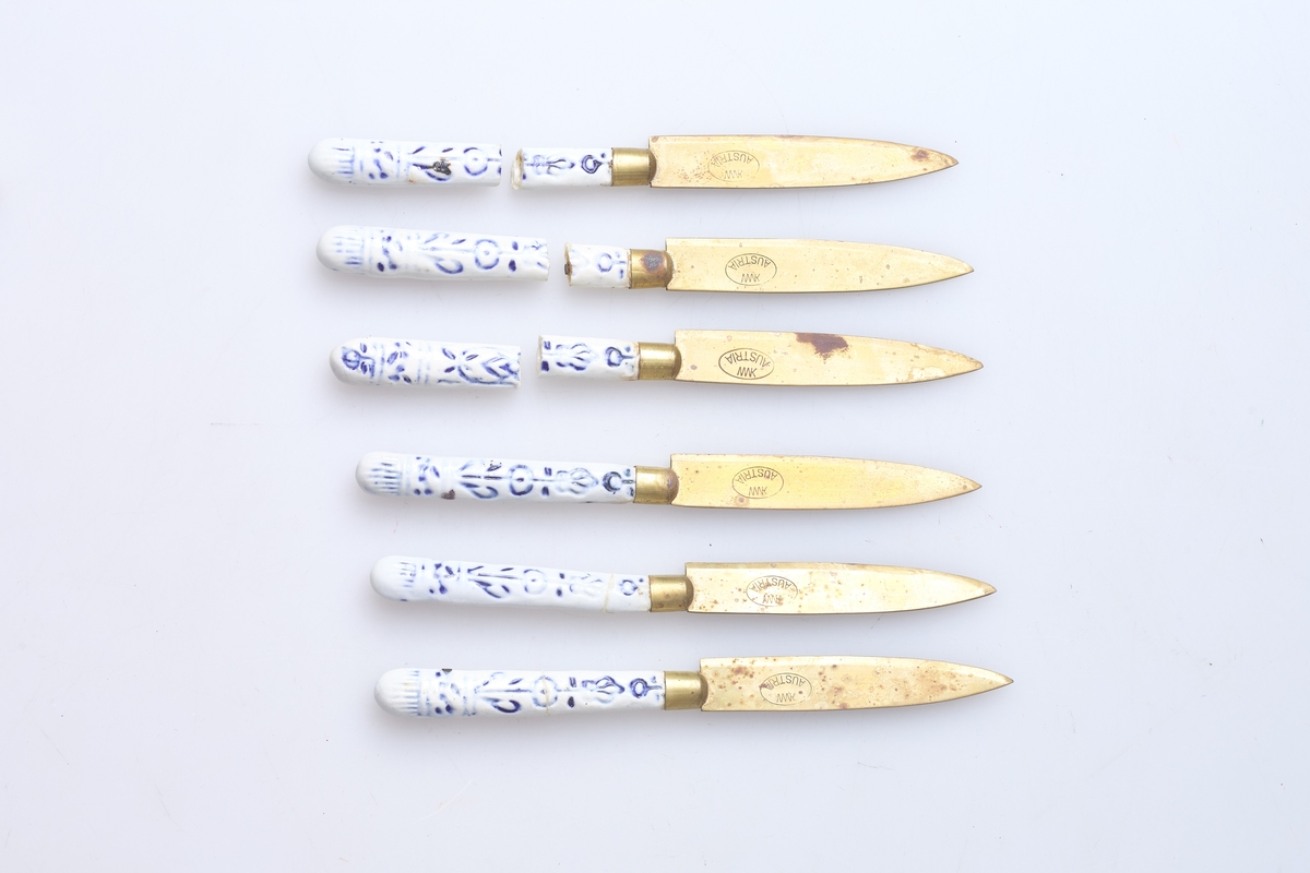 Seks fruktkniver med porselenskaft og messingblad. Skaftet er hvitt med blå dekor, en type dekor på hver side. To av knivene er reparert tidligere og tre av dem er i stykker nå.